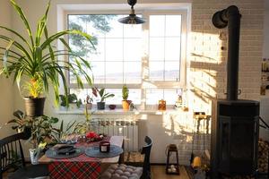 solig interiör av en loftstil hus med inlagd växter, en stor fönster, en täckt tabell för de jul och ny år högtider foto