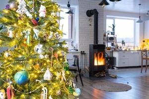 festlig interiör av hus är dekorerad för jul och ny år i loft stil med svart spis, öppen spis, jul träd. värma studio rum med uppsättning tabell, brinnande trä, mysigt och uppvärmning av Hem foto