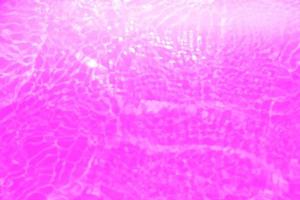 defokusering suddig transparent lila färgad klar lugna vatten yta textur med stänk och bubblor. trendig abstrakt natur bakgrund. vatten vågor i solljus med kopia Plats. rosa vatten släppa glans foto