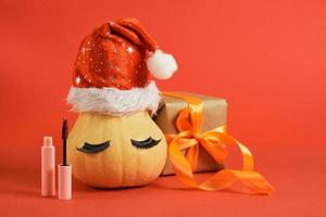 mascara i rosa mock-up förpackning, insvept jul gåvor och pumpa i santa hatt och falsk ögonfransar foto