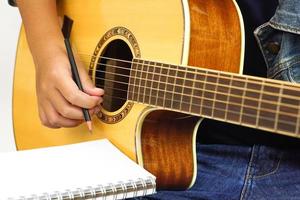 fokus på de händer av de barn eller tonåring spelar akustisk gitarr med ha en penna och anteckningsbok för tar anteckningar. inlärning, öva och koppla av begrepp. foto