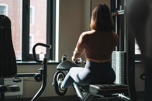 ung kondition brunett kvinna Träning för hand och ben muskler Utrustning på Gym foto