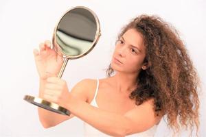 ung kvinna i främre av de spegel kontroll henne ansikte hud foto