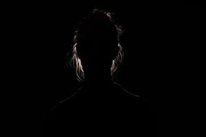 bakgrundsbelyst porträtt silhuett av oigenkännlig kvinna dölja ansikte och identitet i de mörk skugga foto