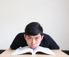 asiatisk ung man uttråkad ansikte med läsa de bok känna sorg på de skrivbord se på kamera isolerad, utbildning begrepp foto