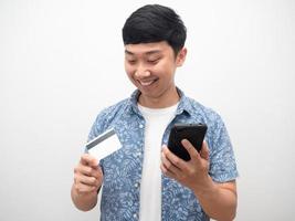 man innehav mobil telefon och ser på kreditera kort i hand Lycklig leende foto