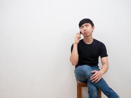asiatisk man Sammanträde på stol talande med cell telefon allvarlig ansikte nad känsla uttråkad på vit bakgrund foto