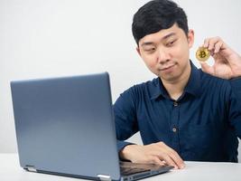 man med bärbar dator på tabell ser på bitcoin i hans hand foto