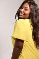 Lycklig mörk flådd kvinna i gul mode klänning. skönhet afro amerikan modell Framställ i studio isolerat på grå bakgrund foto