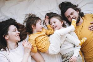 ung Lycklig familj med två barn flickor på säng på de mysigt Hem, se från topp foto