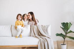 ung Lycklig familj med ett förälder kvinna mor med två barn flickor på soffa i levande rum med grön hus växt på Hem foto