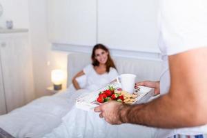 vård och roman på de morgon. överraskad och Lycklig ung kvinna liggande på de säng med manlig händer föra frukost. Bra morgon- friska frukost i säng. foto