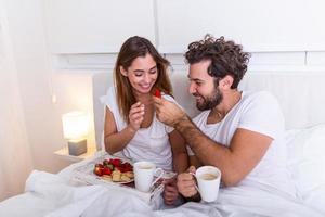 par i kärlek har frukost i säng. ung caucasian par har romantisk frukost i säng. kvinna och manlig , två koppar av kaffe, frukt och färgrik kex. foto