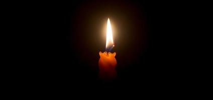 en enda brinnande ljus flamma eller ljus lysande på en skön spiral orange ljus på svart eller mörk bakgrund på tabell i kyrka för jul, begravning eller minnesmärke service med kopia Plats foto