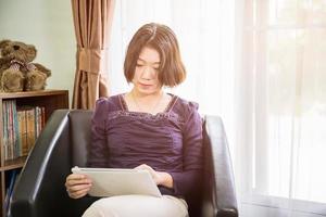 ung asiatisk kvinna kort hår använda sig av mobil telefon i levande rum foto