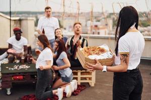 med utsökt pizza. grupp av ung människor i tillfällig kläder ha en fest på taket tillsammans på dagtid foto