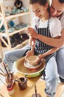 med henne pojkvän eller Make. ung kvinna keramiker ha en Arbetar inomhus med handgjort lera produkt. uppfattning av krukmakeri foto