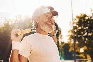 skön solljus. senior eleganta man i vit skjorta och svart sportigt shorts på tennis domstol foto