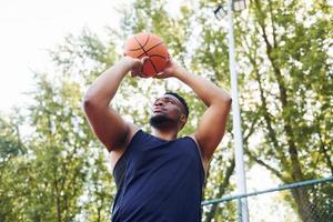 molnig väder. afrikansk amerikan man spelar basketboll på de domstol utomhus foto