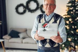 fira ny år och stående nära jul träd. senior man i trevlig kläder är på Hem foto