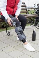kvinna bär knä spänna eller ortos efter ben kirurgi, gående i de parkera foto