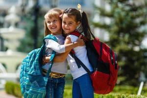 två skola flickor bär ryggsäck utanför de primär skola. skolflicka, elementärt skola studerande gående från skola, gradering, sommar högtider. foto