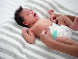 söt bebis flicka gråt medan henne mor ändrats henne blöja. blandras asiatisk-australisk spädbarn klänning upp efter badning förbi henne mamma. hälsa vård begrepp. foto