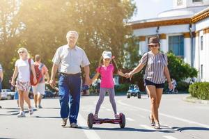 liten leende flicka inlärning till rida en hoverboard med henne föräldrar utomhus foto