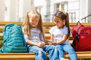 barn gående till skola. två flickor innehav böcker och pennor på de först skola dag. liten studenter upphetsad till vara tillbaka till skola. början av klass efter semester. foto