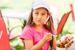 skön liten flicka äter en bubbla våffla med is grädde i de sommar foto