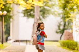 liten flicka gående in i skola med ryggsäck i de morgon- under värma solsken. utbildning begrepp. foto