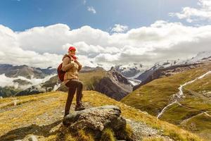 ung Lycklig kvinna med ryggsäck stående på en sten och ser till en dal Nedan foto