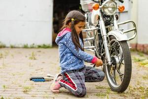 liten flicka reparation en motorcykel, studerande flicka i motorcykel mekanik foto
