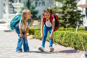 två skola flickor bär ryggsäck utanför de primär skola. skolflicka, elementärt skola studerande gående från skola, gradering, sommar högtider. foto