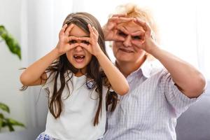 förtjusande lekfull liten barn flicka med Lycklig mitten åldrig barnskötare mormor på Hem. söt små förskola barnbarn med upphetsad äldre mormor. foto