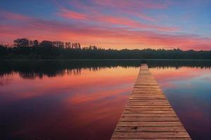 color trä- pir på en sjö den där är totalt lugna under solnedgång foto