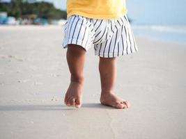 stänga upp fötter av unge gående på de strand med skön hav bakgrund foto