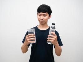 positiv asiatisk man ser på glas med vatten flaska i hand foto