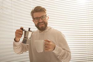 ung man häller kaffe från moka pott på morgon. frukost och ha sönder begrepp. foto