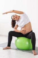 en ung gravid kvinna håller på med övning använder sig av en kondition boll medan Sammanträde på en matta. foto