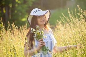 ung kvinna plockning blommor i de äng i sommar kväll foto