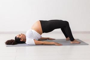ung flexibel gravid kvinna håller på med gymnastik på matta på de golv på vit bakgrund. de begrepp av framställning de kropp för lätt förlossning foto
