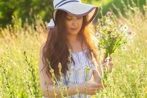 ung kvinna plockning blommor i de äng i sommar kväll foto