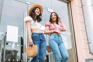 Lycklig leende skön brunett ung kvinnor vänner i sommar kläder gående på de sommar stad gata, detaljhandeln handla foto