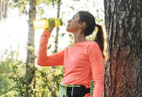 ung smal kvinna brunett i sport kläder löpning och dricka vatten på skog på gyllene timme soluppgång tid. hälsa och friskvård, kondition livsstil foto