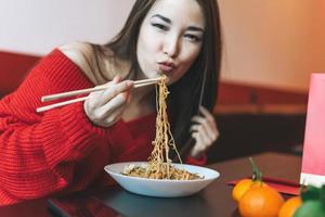 skön leende ung asiatisk kvinna i röd kläder äter asiatisk mat med bambu ätpinnar i de kinesisk vietnamese restaurang foto