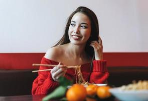 skön leende ung asiatisk kvinna i röd kläder äter asiatisk mat i de kinesisk vietnamese restaurang foto