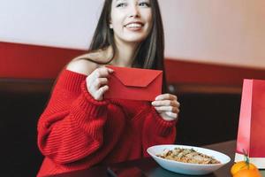 skön ung asiatisk kvinna i röd kläder äter asiatisk mat med röd kuvert i restaurang fira kinesisk ny år foto