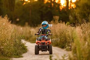 en liten pojke bär en hjälm ridning en quad cykel på de Strand av en berg flod. foto