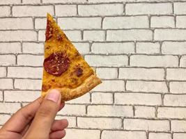 hand hölls pizza skiva mot vit tegel vägg bakgrund foto